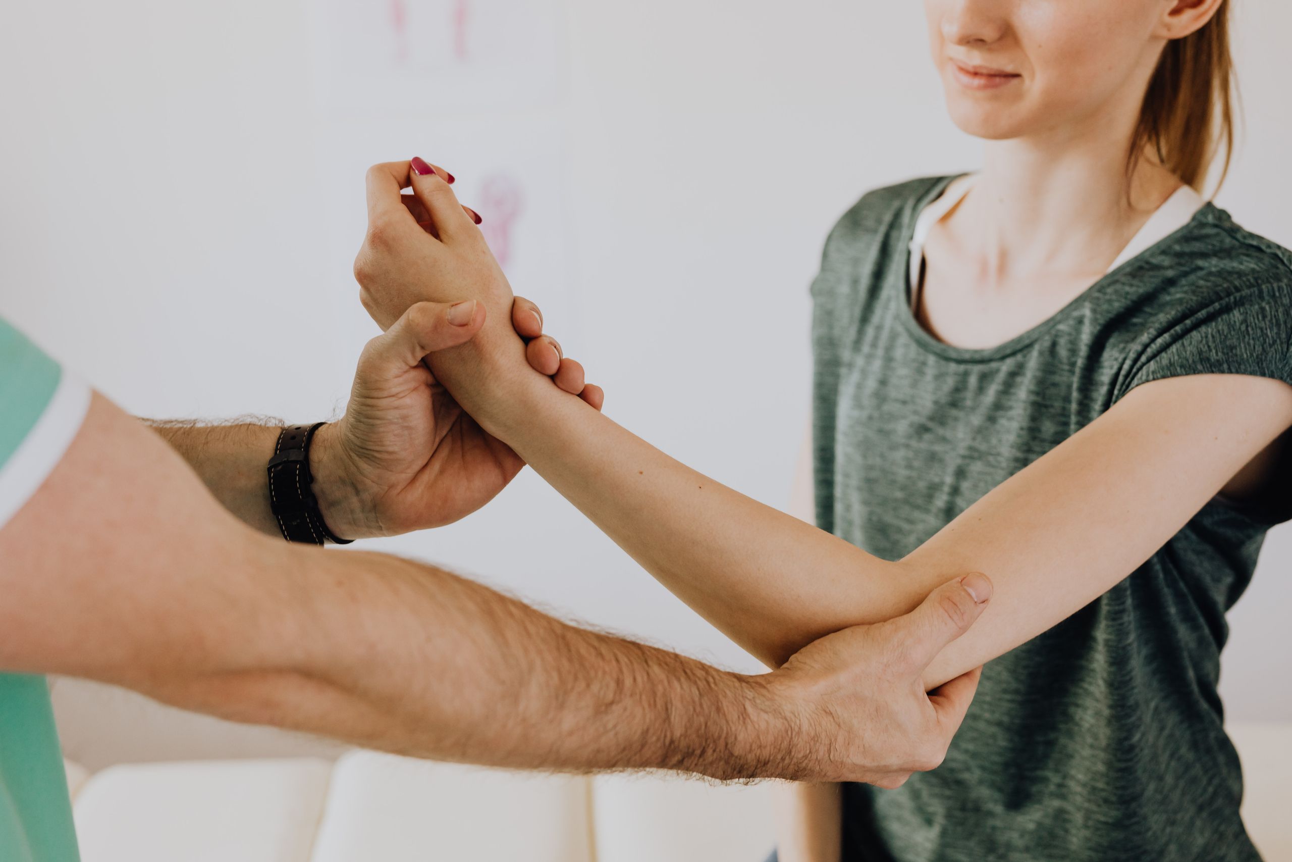 Crop faceless orthopedist in uniform and wristwatch checking up arm joint of slim woman in casual wear in doctor office in clinic